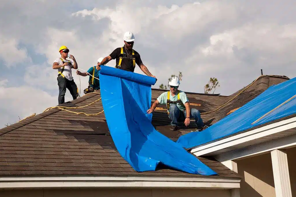 24/7 emergency roof repair team from a Peoria roofing company applying a blue protective tarp to a storm-damaged home.