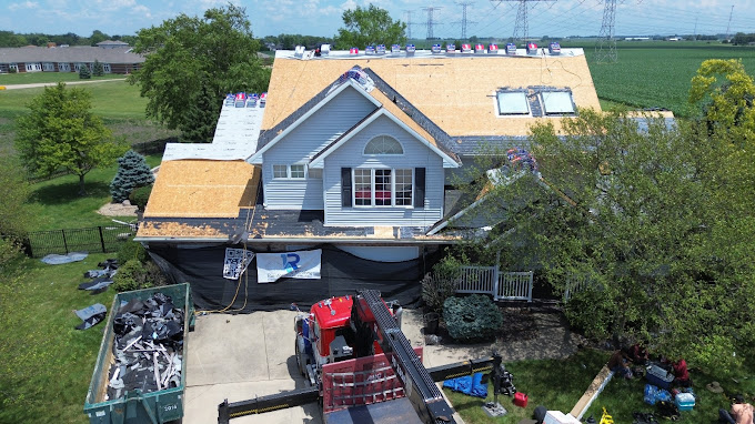 Aerial drone view of a professional roofing company crew performing a full residential roof replacement in Peoria, IL