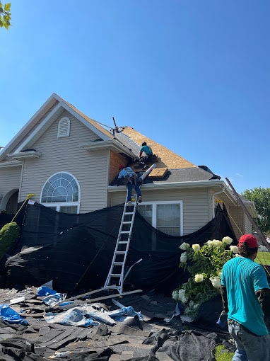 Roofing company crew utilizing professional safety equipment and debris management while replacing a steep residential roof.