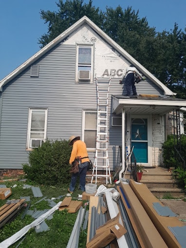 Skilled siding contractor team from a professional Peoria roofing company installing new gray vinyl siding on a two-story home.