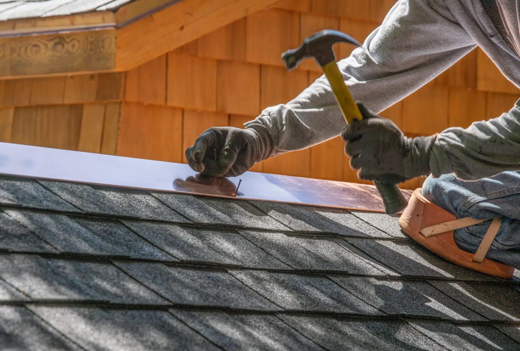 Detailed view of a roofer from an expert roofing company precisely installing metal flashing and shingles to meet manufacturer specifications.