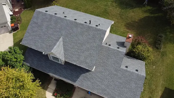 Blog 12 Close-up aerial drone shot of a gray asphalt shingle roof showing a dormer window and copper chimney cap