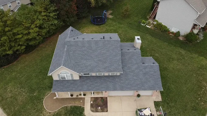 Aerial drone view of a two-story home's blue-gray asphalt shingle roof with a backyard trampoline visible