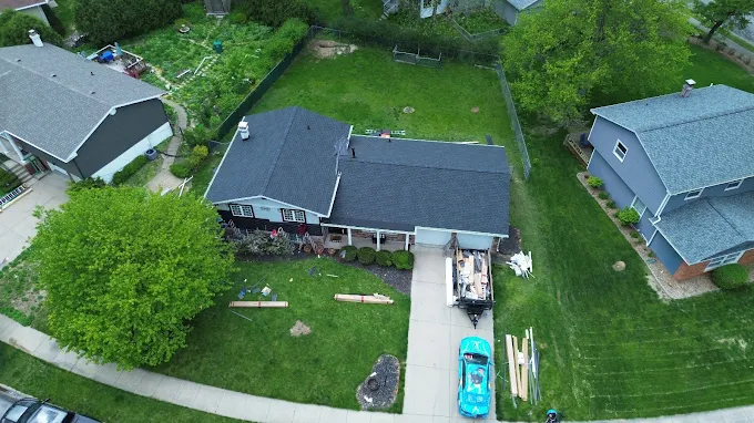 Drone inspection view of a ranch-style home's dark gray shingle roof with a full driveway view of the property