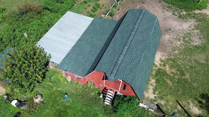 Aerial drone image of a red barn showing a metal roof mid-replacement, half old panels and half new green metal roofing