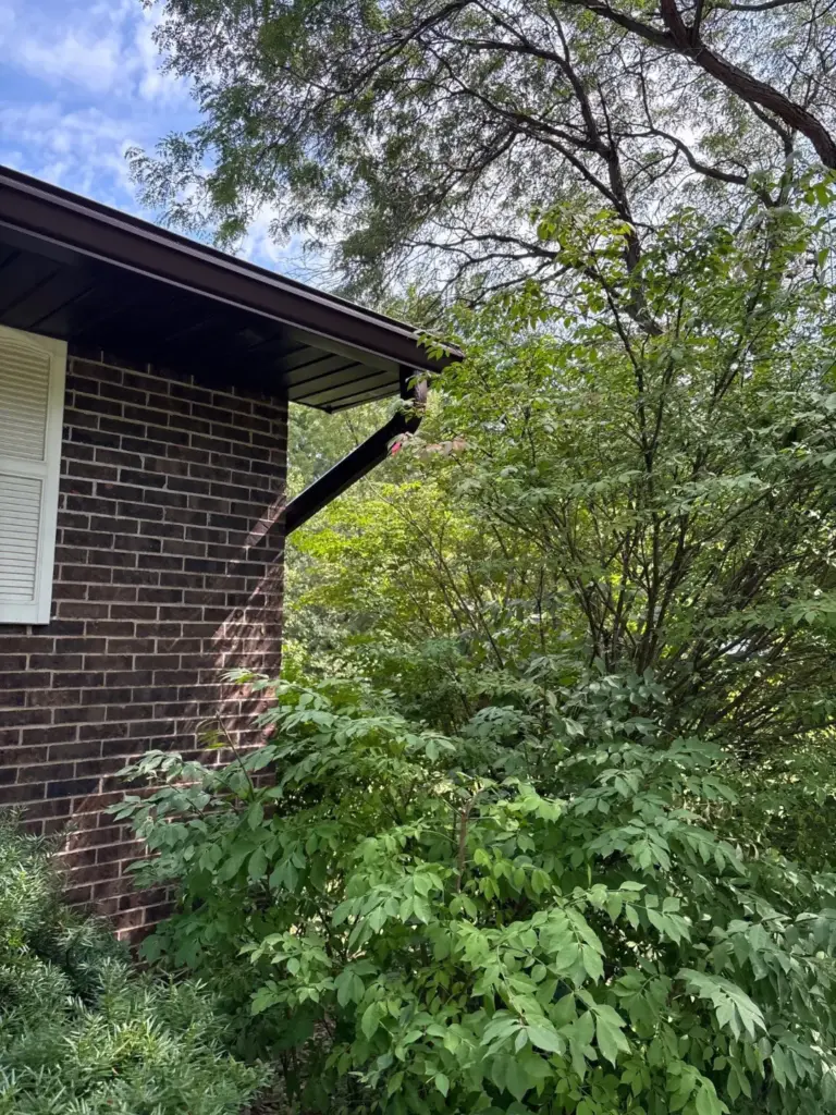 Underside of a new brown gutter and soffit on a brick home with a wooden deck and folding chairs