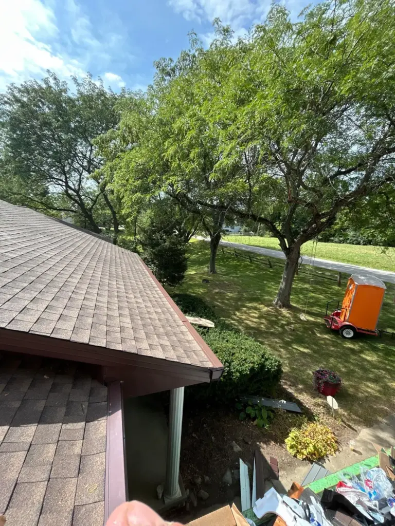 New asphalt shingles and brown drip edge along a roof eave with a portable restroom trailer on the lawn