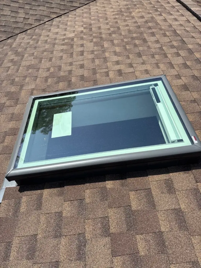Close-up of a roof skylight with metal frame and flashing set into brown architectural shingles