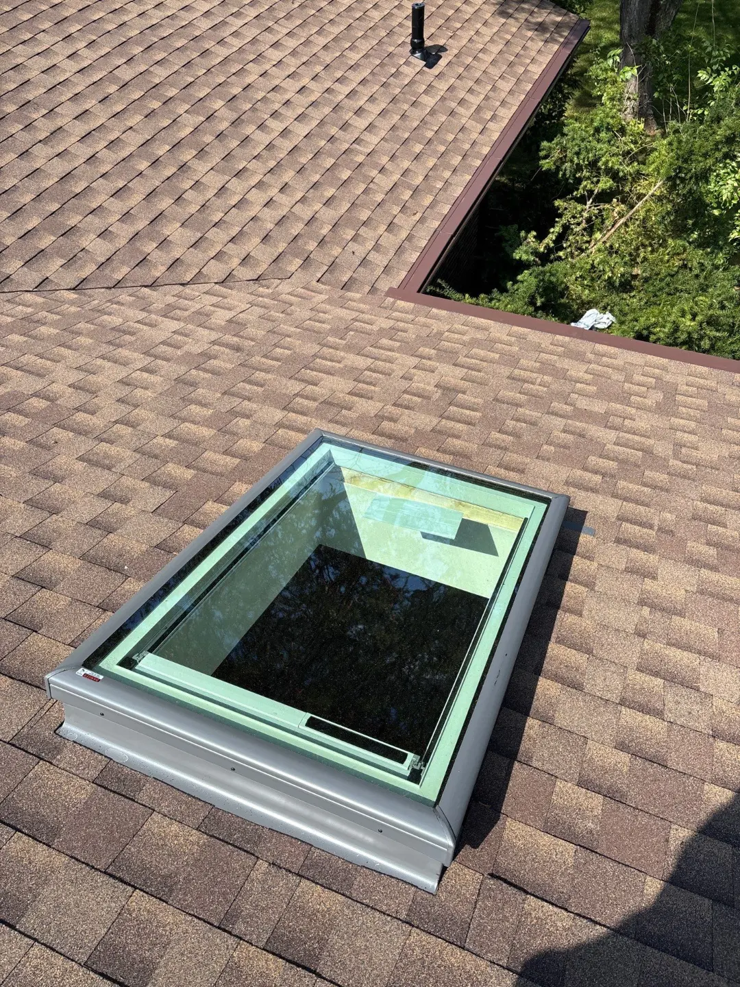 Skylight on a newly shingled roof with a ridge vent and brown fascia trim in the background
