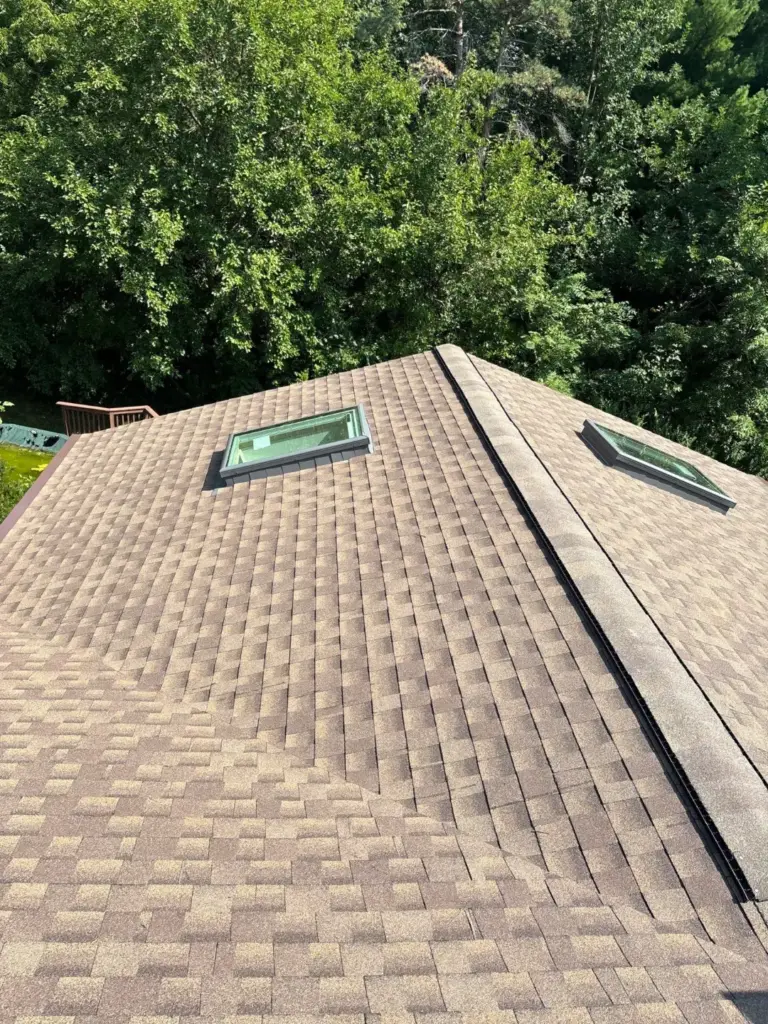 Roof slope with two skylights, new shingles and a capped ridge vent above a tree-lined backyard